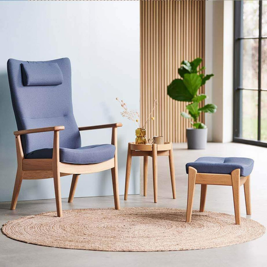 Dansk design lænestol i eg med blå stof og tilhørende skammel ved siden af små sideborde og grøn plante i stuen