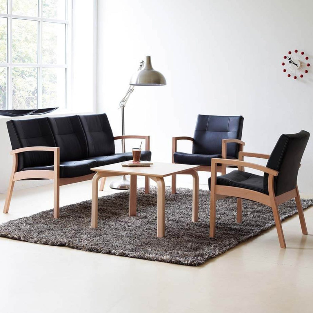 Et moderne møbelsæt med lænestole i egetræ betrukket med sort læder og tilhørende sofa omkring et træbord i lyst rum med naturligt lys og minimalistisk indretning.
